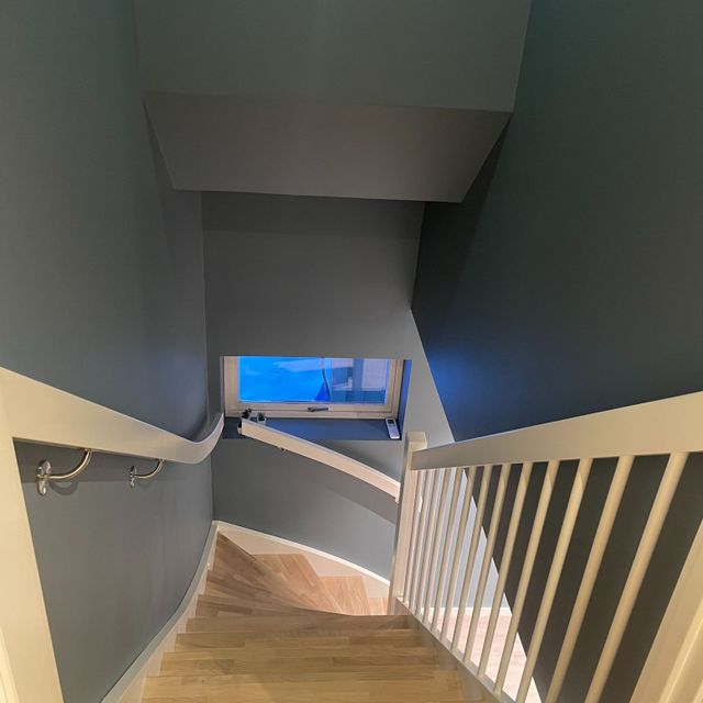 Trapp i lyst og hvitmalet tre i dus blå trappeoppgang sett fra overetasje